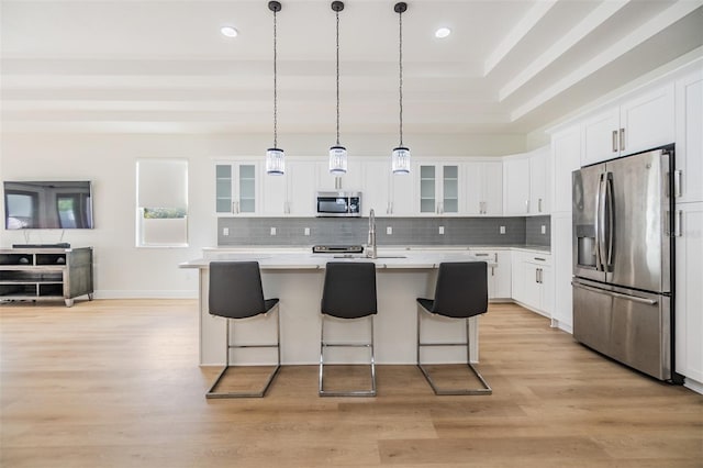 kitchen with appliances with stainless steel finishes, a breakfast bar, light hardwood / wood-style floors, white cabinetry, and an island with sink