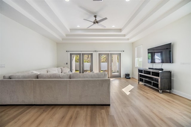 living room featuring a tray ceiling, ceiling fan, french doors, and light wood-type flooring