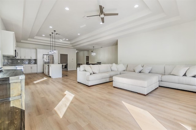 living room with ceiling fan, a raised ceiling, and light hardwood / wood-style flooring