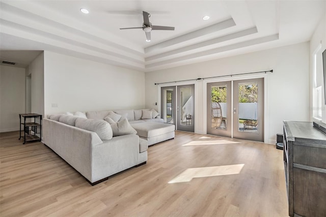 living room with a tray ceiling, ceiling fan, french doors, and light hardwood / wood-style floors