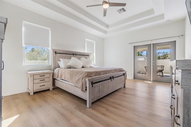 bedroom with ceiling fan, french doors, light hardwood / wood-style flooring, a tray ceiling, and access to outside