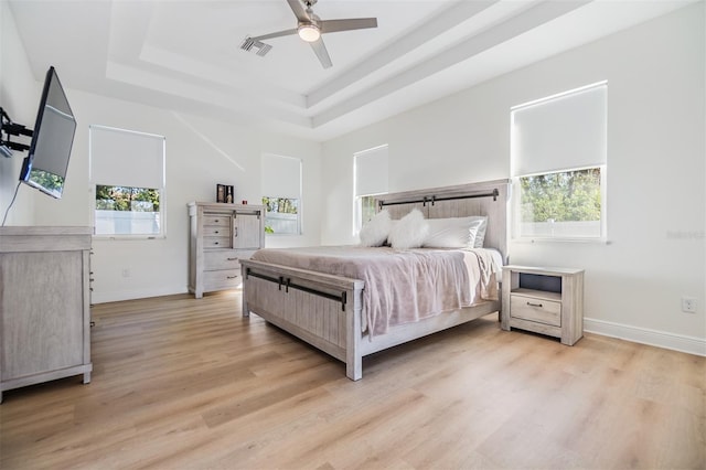 bedroom featuring a raised ceiling, multiple windows, ceiling fan, and light hardwood / wood-style flooring