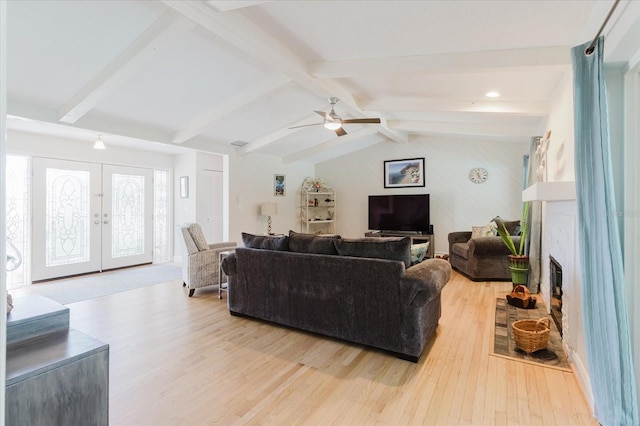 living room featuring vaulted ceiling with beams, light wood-style floors, a glass covered fireplace, and french doors