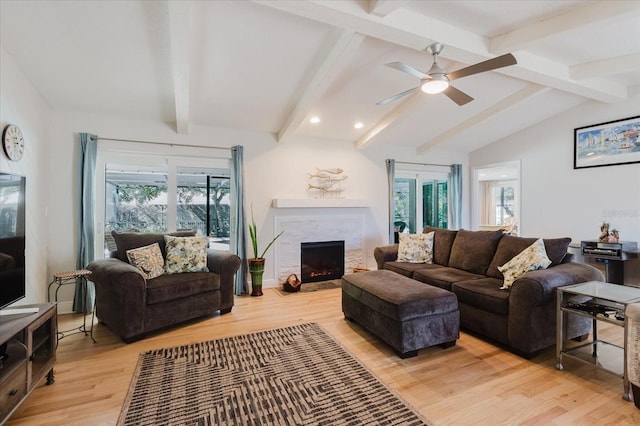 living room featuring lofted ceiling with beams, light wood finished floors, a fireplace, and a ceiling fan