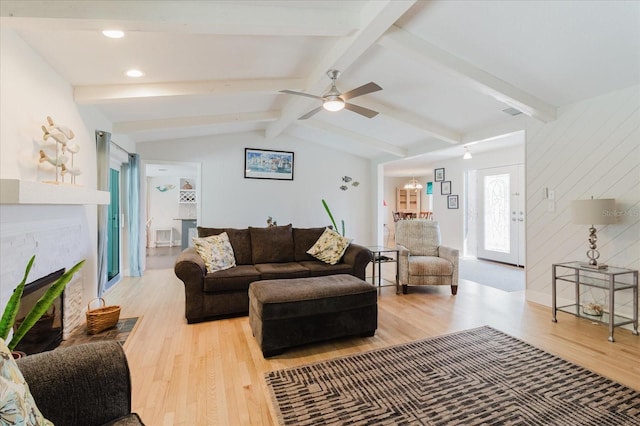 living room with vaulted ceiling with beams, ceiling fan, a brick fireplace, and light wood-style floors