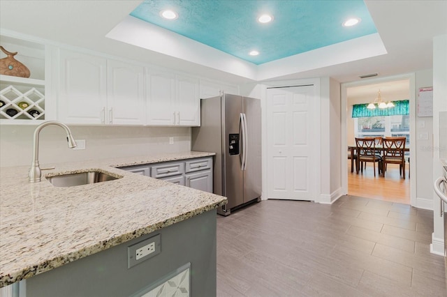 kitchen with stainless steel fridge, white cabinets, light stone countertops, a tray ceiling, and a sink