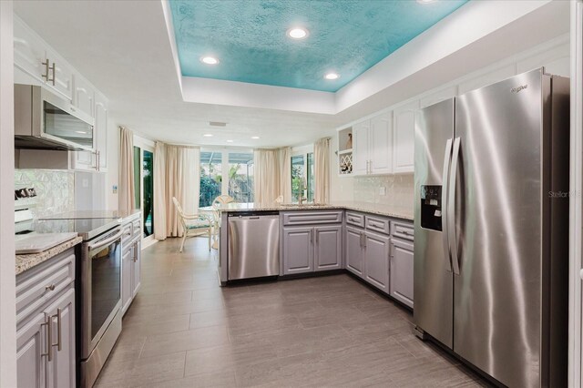 kitchen with appliances with stainless steel finishes, a tray ceiling, backsplash, and a peninsula