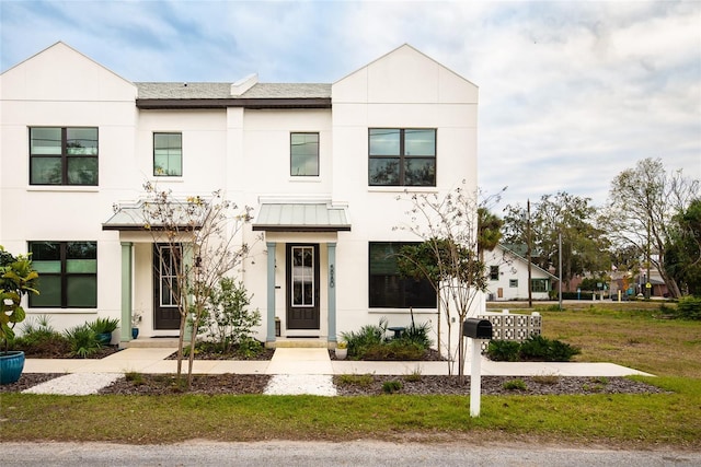 view of front of house featuring a front yard, a standing seam roof, metal roof, and stucco siding