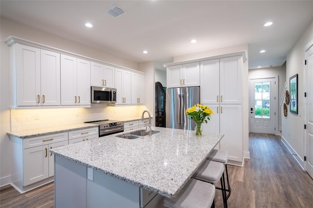 kitchen with appliances with stainless steel finishes, a sink, a kitchen island with sink, and white cabinetry