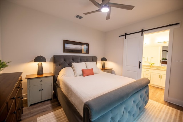 bedroom with ceiling fan, a barn door, hardwood / wood-style floors, and ensuite bath