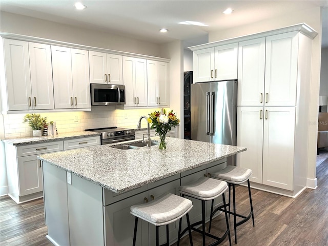 kitchen featuring an island with sink, appliances with stainless steel finishes, light stone counters, white cabinetry, and a sink