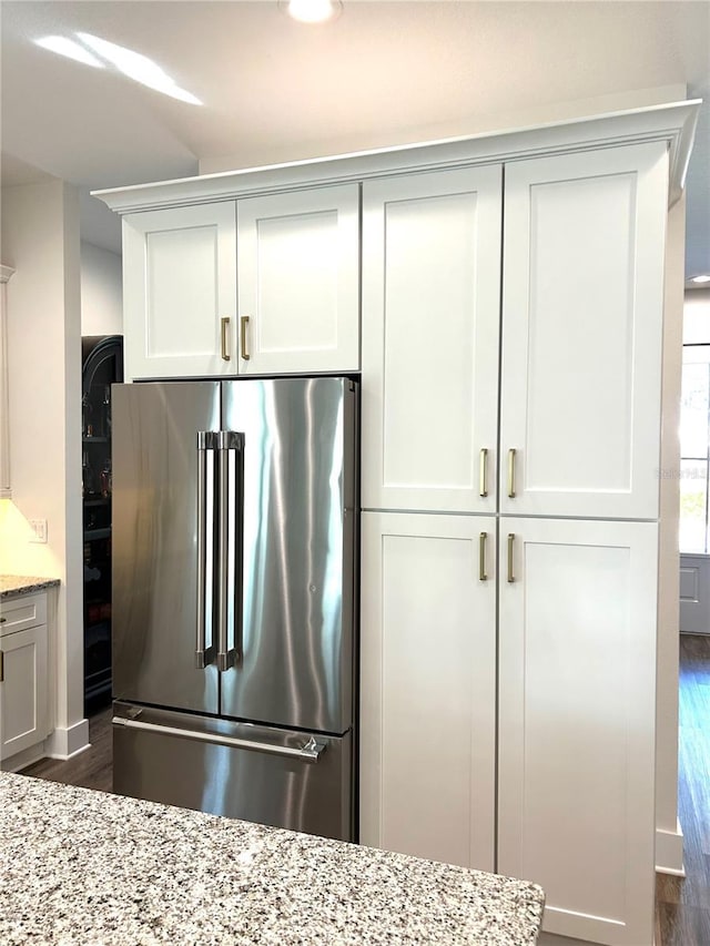 kitchen featuring dark hardwood / wood-style flooring, light stone counters, high end refrigerator, and white cabinetry