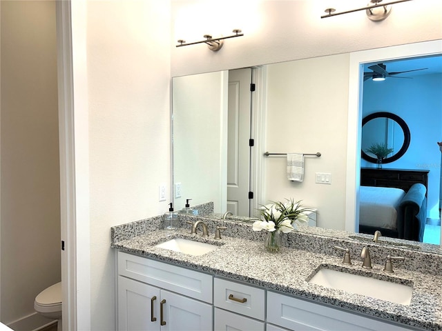 ensuite bathroom with double vanity, a sink, toilet, and connected bathroom