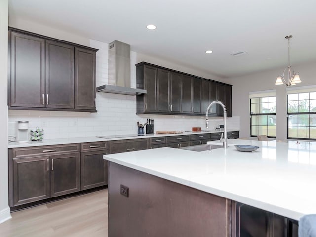 kitchen with tasteful backsplash, dark brown cabinetry, black electric cooktop, wall chimney range hood, and a notable chandelier