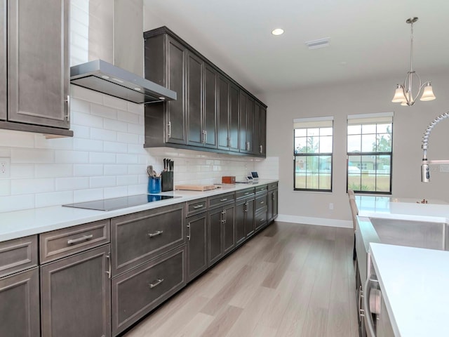 kitchen with black electric stovetop, wall chimney exhaust hood, dark brown cabinets, light hardwood / wood-style flooring, and hanging light fixtures