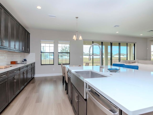 kitchen with tasteful backsplash, a kitchen island with sink, pendant lighting, light hardwood / wood-style flooring, and dishwasher