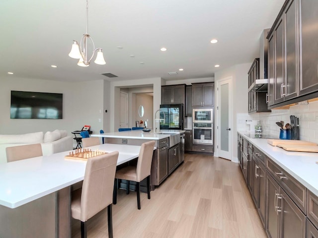 kitchen featuring stainless steel oven, a kitchen island with sink, a kitchen breakfast bar, tasteful backsplash, and decorative light fixtures