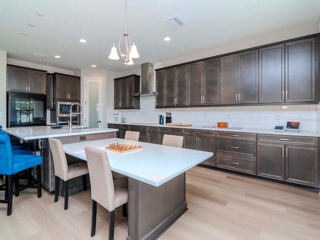 kitchen with a center island with sink, a kitchen breakfast bar, wall chimney range hood, decorative light fixtures, and dark brown cabinets