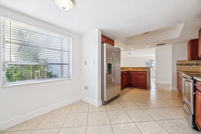 kitchen with kitchen peninsula, light stone counters, stainless steel appliances, a tray ceiling, and light tile patterned flooring