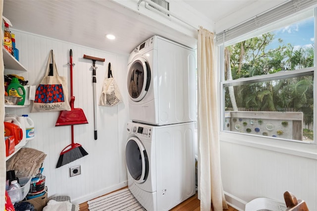 clothes washing area featuring stacked washer / dryer, wood walls, and light hardwood / wood-style flooring