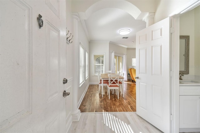 hallway featuring light hardwood / wood-style floors, crown molding, ornate columns, and sink