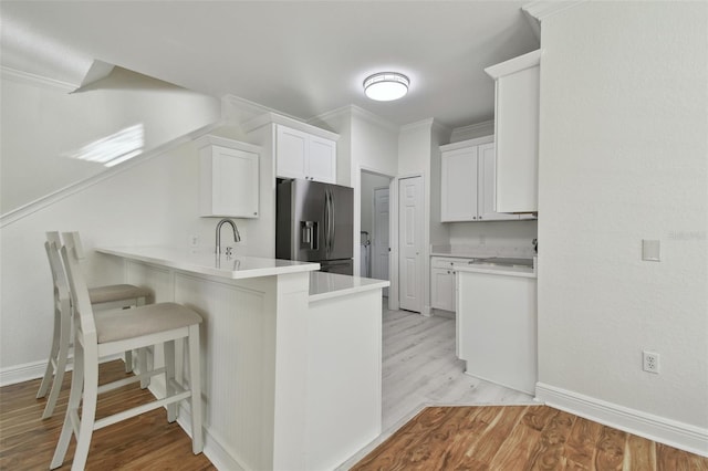 kitchen with stainless steel fridge with ice dispenser, kitchen peninsula, a breakfast bar, white cabinets, and light wood-type flooring