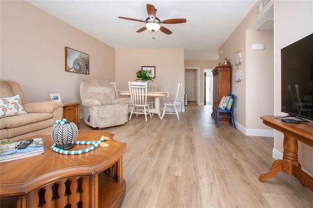 living room featuring light wood finished floors, a ceiling fan, visible vents, and baseboards