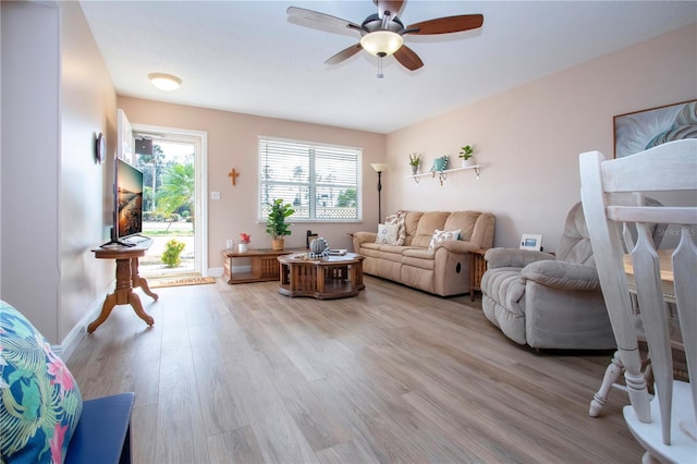 living area with light wood finished floors, a ceiling fan, and baseboards