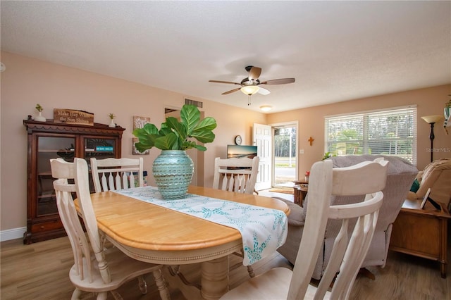 dining space featuring baseboards, ceiling fan, a textured ceiling, and light wood finished floors