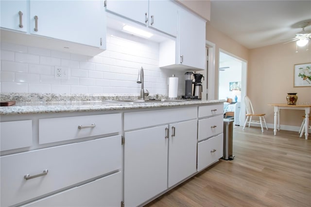 kitchen with light wood finished floors, white cabinets, ceiling fan, backsplash, and a sink