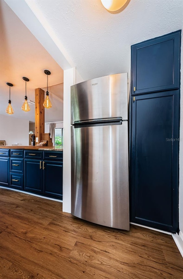 kitchen with lofted ceiling, blue cabinets, dark hardwood / wood-style floors, decorative light fixtures, and stainless steel refrigerator