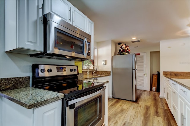 kitchen featuring light wood-type flooring, dark stone counters, stainless steel appliances, sink, and white cabinetry