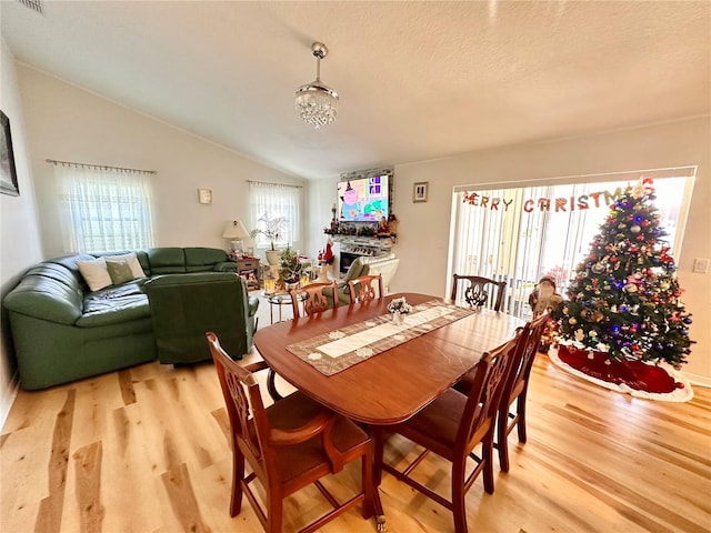 dining room featuring light hardwood / wood-style floors, lofted ceiling, a textured ceiling, and a chandelier