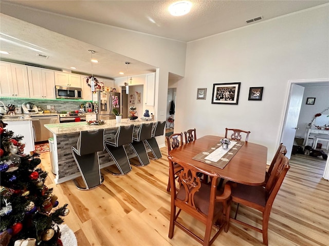 dining room with a textured ceiling, light wood-type flooring, and vaulted ceiling