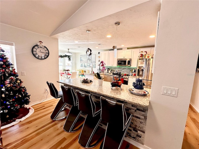 kitchen featuring light stone countertops, appliances with stainless steel finishes, kitchen peninsula, decorative light fixtures, and light hardwood / wood-style flooring