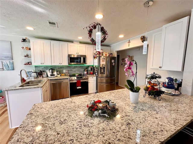 kitchen with white cabinetry, sink, stainless steel appliances, kitchen peninsula, and decorative light fixtures