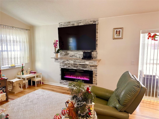 living room with a textured ceiling, a stone fireplace, hardwood / wood-style floors, and vaulted ceiling