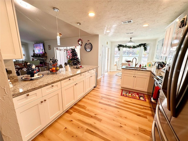 kitchen with light stone counters, a textured ceiling, sink, pendant lighting, and stainless steel fridge with ice dispenser