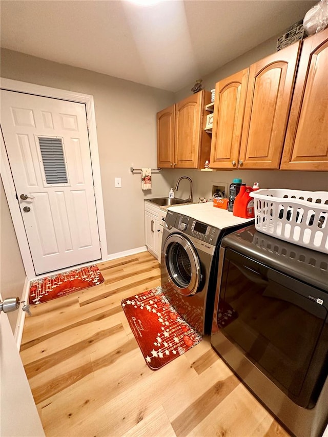 laundry area featuring washer and clothes dryer, cabinets, light wood-type flooring, and sink