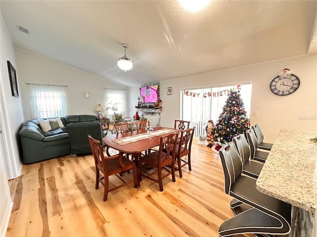 dining room with a textured ceiling, light hardwood / wood-style flooring, and lofted ceiling