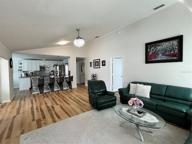 living area featuring light wood finished floors, visible vents, and lofted ceiling