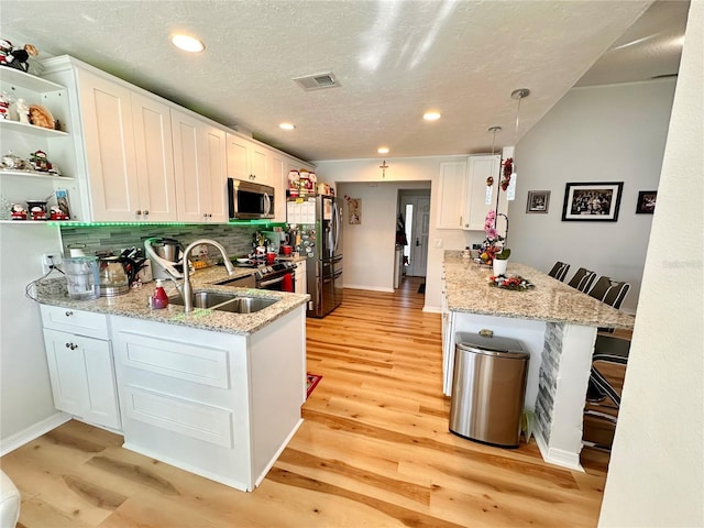kitchen with light wood-style floors, stainless steel appliances, visible vents, a peninsula, and backsplash