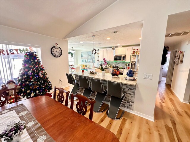 dining space with baseboards, vaulted ceiling, and light wood-type flooring