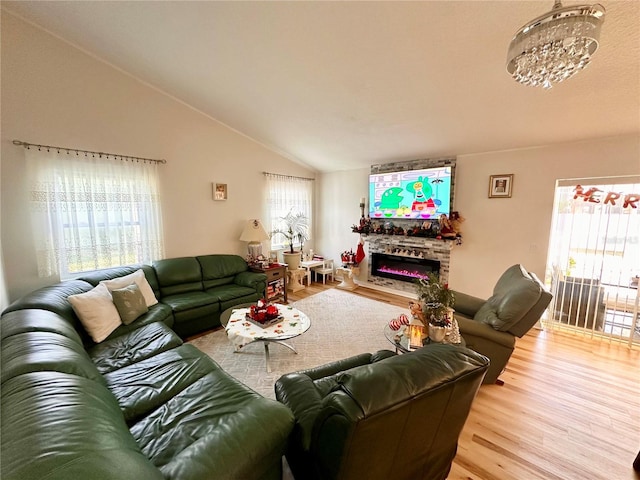living area featuring lofted ceiling, wood finished floors, a fireplace, and a notable chandelier