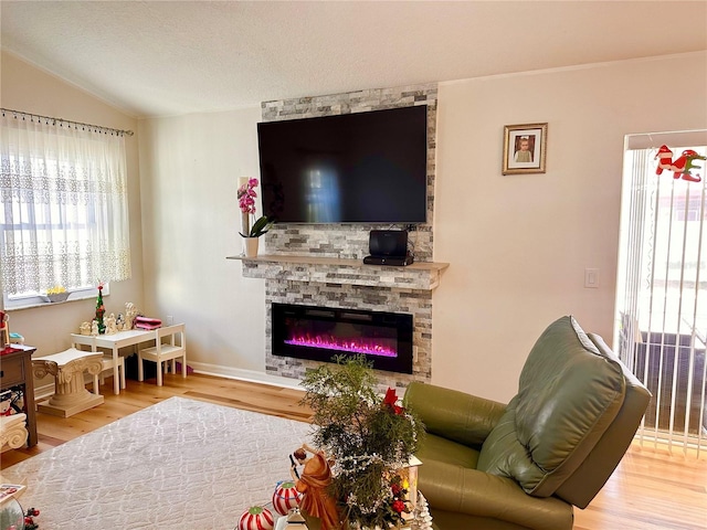 living room with wood finished floors, a stone fireplace, a textured ceiling, and vaulted ceiling