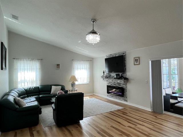 living area featuring lofted ceiling, visible vents, a stone fireplace, baseboards, and wood finished floors