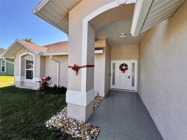 view of exterior entry featuring stucco siding and a lawn
