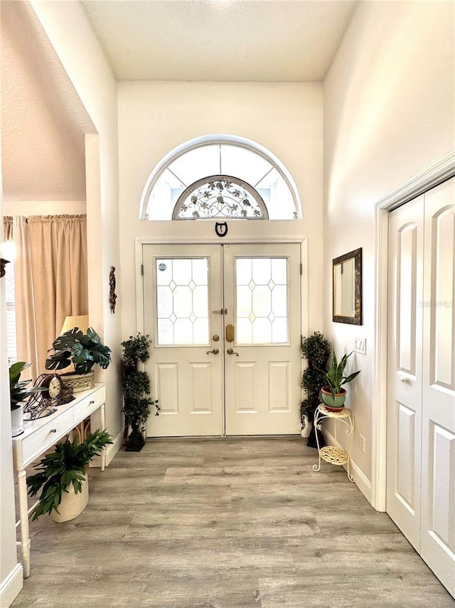 foyer entrance with french doors, a towering ceiling, and light hardwood / wood-style flooring