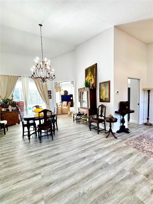 dining room featuring a notable chandelier, a high ceiling, a textured ceiling, and light wood-type flooring