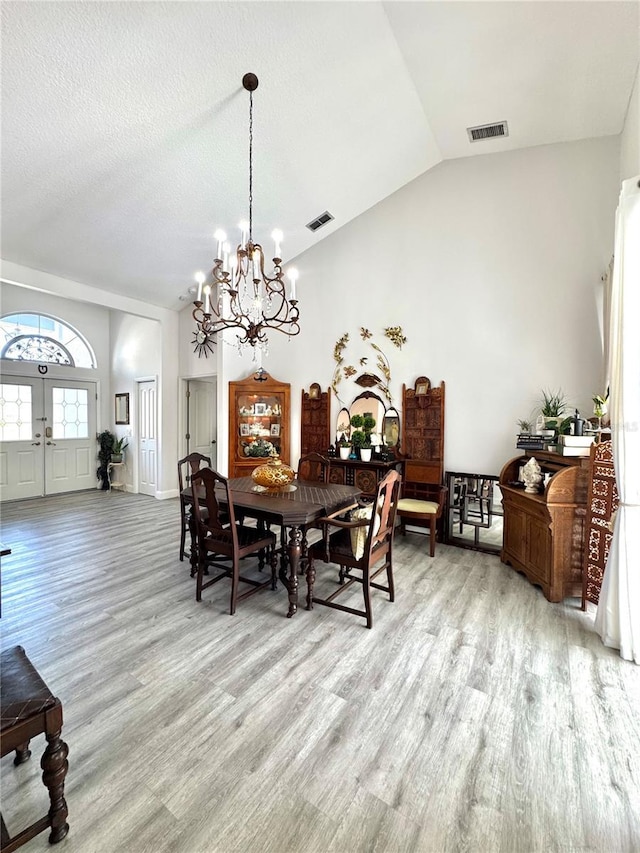 dining area featuring lofted ceiling, light hardwood / wood-style floors, a textured ceiling, and a notable chandelier